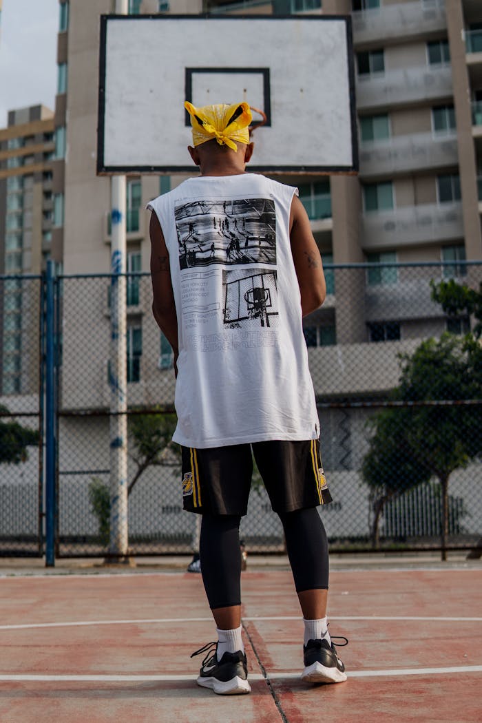 Home Rear view of a man in sports attire standing on an outdoor basketball court, ready to play.