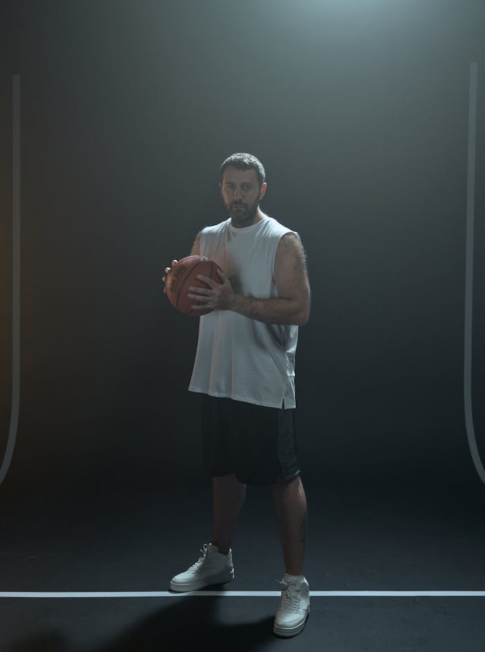About Portrait of a basketball player holding a ball in a dimly lit studio setting.